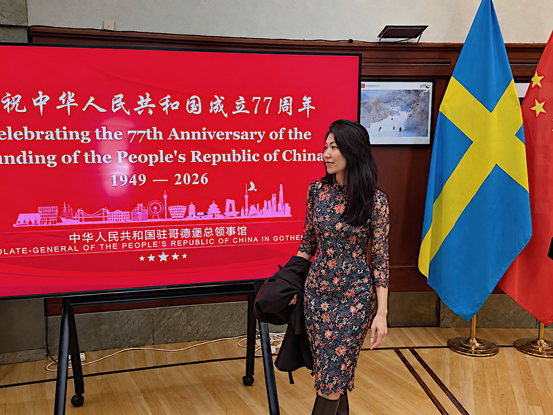 Cheryl Marie Cordeiro at the Consulate-General of the People’s Republic of China in Gothenburg, beside the 77th anniversary screen and the Swedish and Chinese flags