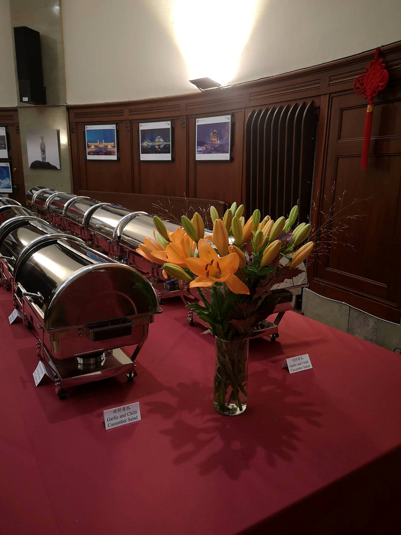 Buffet table with chafing dishes and a vase of orange lilies on a red tablecloth